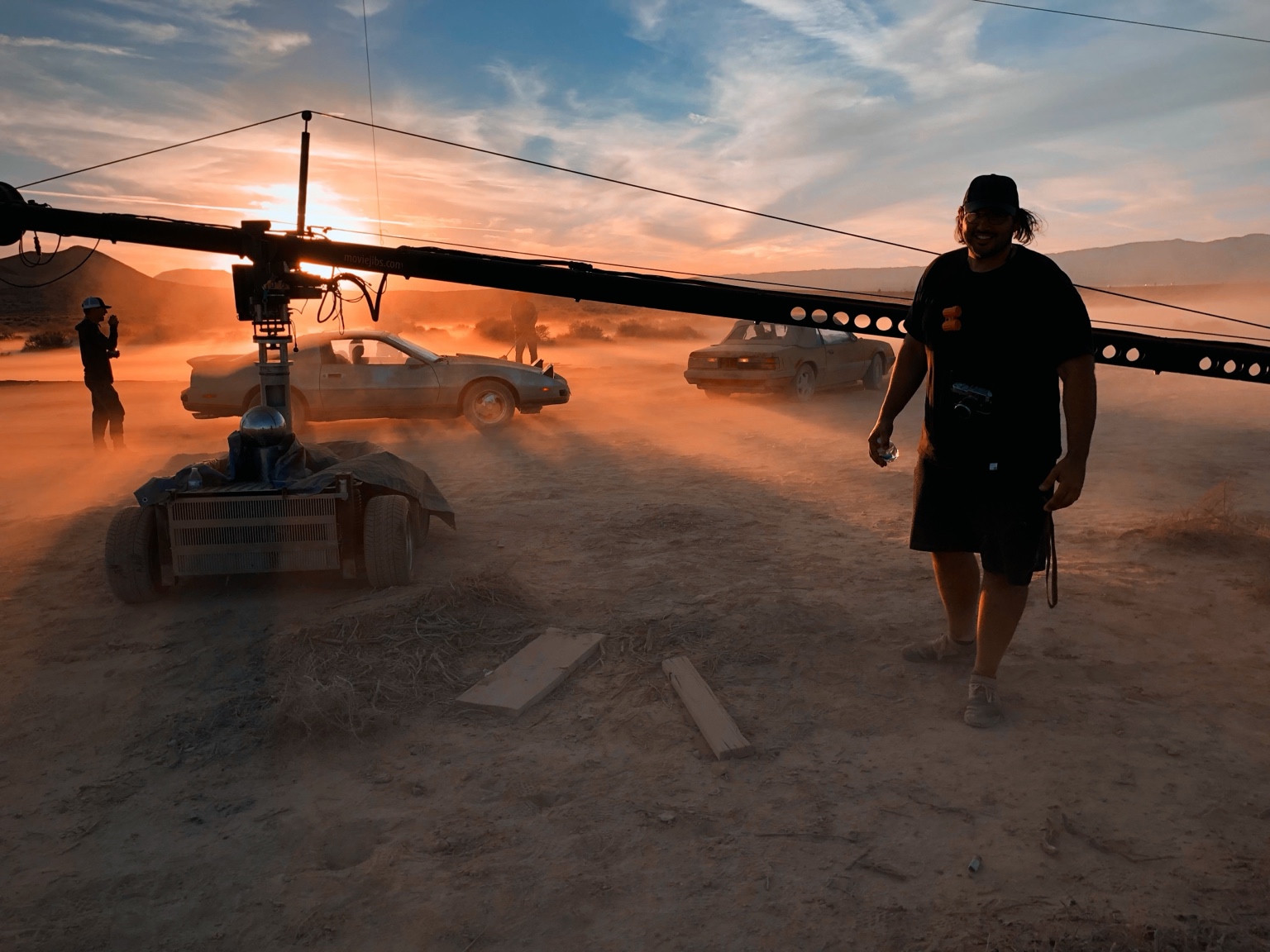 Behind the scenes in the desert at sunset, with cars in dust and the camera jib in the foreground