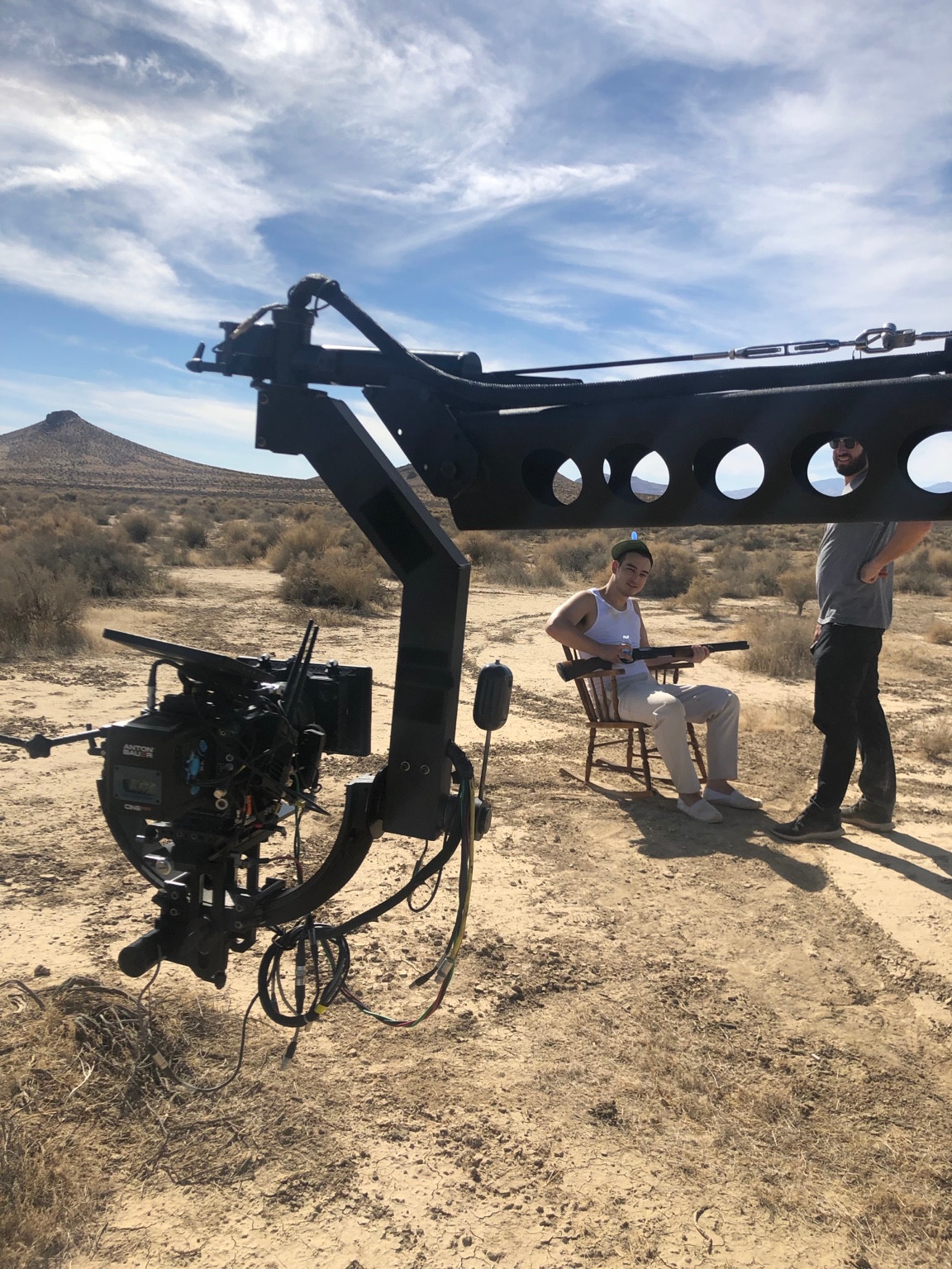 Behind the scenes: Joji in a propeller hat, seated in a rocking chair holding a gun, beside the camera jib
